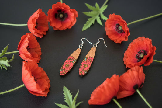 A pair of handmade wooden dangle earrings with a pink floral pattern and silver fishhook wires, displayed on a dark textured surface.
