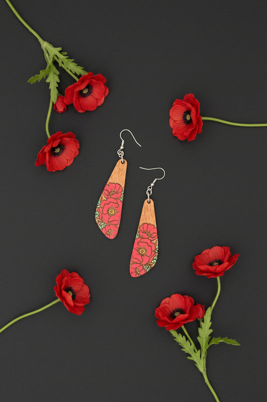 A pair of wooden dangle earrings with a natural wood top half and a red floral patterned bottom half, hanging on silver fishhook wires against a dark textured background.